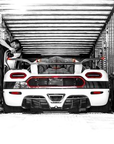 a man standing next to a white sports car in a storage area with it's doors open