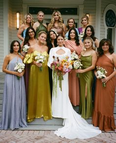 a group of women standing next to each other in front of a white house wearing dresses