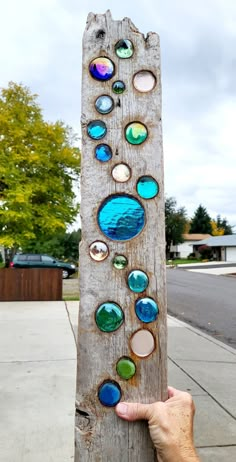 a person holding up a piece of wood with different colored glass buttons on it