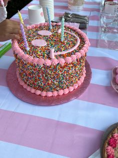 a birthday cake with sprinkles and candles on a pink and white table cloth