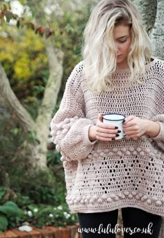 a woman standing next to a tree holding a coffee cup