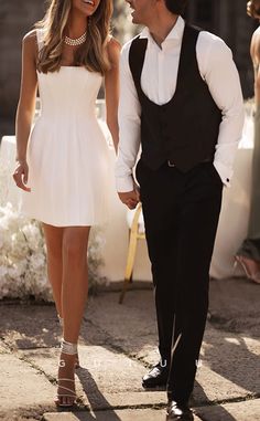 a man in a tuxedo and a woman in a white dress holding hands