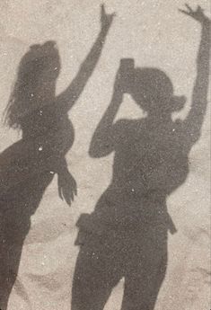 two people are standing in the sand with their hands up