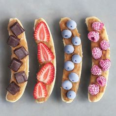 four different types of desserts are arranged in a row on a gray surface with blueberries, strawberries, and chocolate