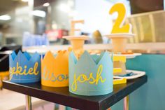 three paper crowns sitting on top of a table in front of a counter with plates and cups