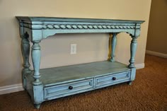 an old blue table with two drawers on the bottom and one drawer below it, in front of a white wall