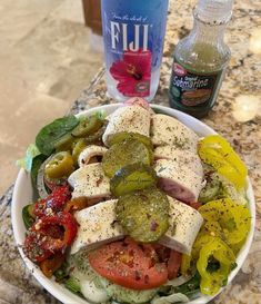 a white bowl filled with lots of different types of vegetables next to a bottle of vodka