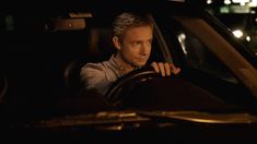 a man sitting in the driver's seat of a car with his hand on the steering wheel