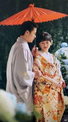 a man and woman standing next to each other under an umbrella in front of flowers