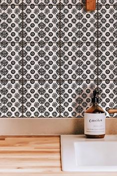 a white sink sitting under a faucet next to a wooden counter top in front of a black and white tiled wall