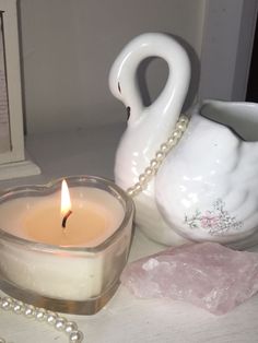 a candle is sitting on a table next to a swan shaped vase and pearl necklace