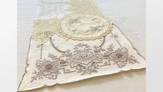 an embroidered piece of cloth with lace and flowers on it, sitting on a white surface