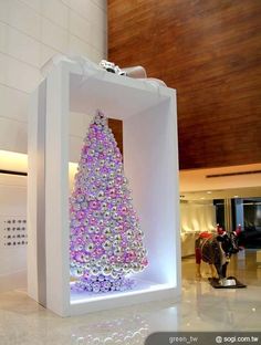 a christmas tree made out of candy in a white box with people walking by it