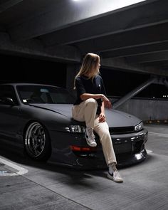 a woman sitting on the hood of a car in an underground parking garage with her legs crossed