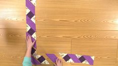 two people are making a purple and white tie out of strips of paper on the floor