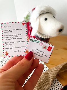 a person holding up two small cards in front of a stuffed dog on a table