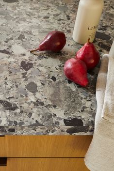 three pears sitting on top of a counter next to a bottle and towel in a kitchen