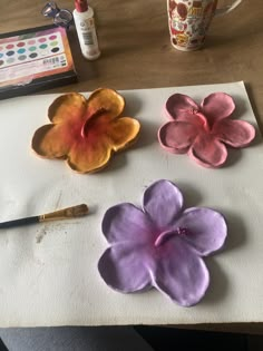 three flowers are sitting on a piece of paper next to a paintbrush and watercolor pencil