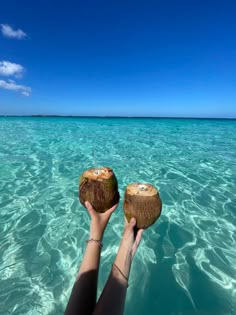 a person is holding two coconuts in the clear blue water on a sunny day