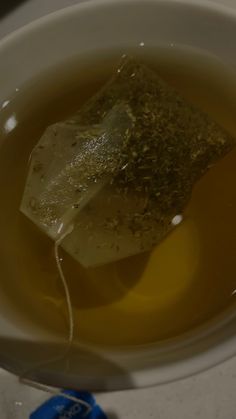 a tea bag in a white cup filled with green tea and some kind of substance