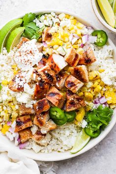 a white bowl filled with chicken and rice next to lime wedges on the side