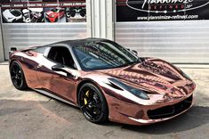 a red and gold sports car parked in front of a garage with two large windows