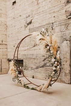 a circular wreath with dried flowers and greenery on the side of a brick wall