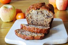 two slices of banana bread on a cutting board with apples and oranges in the background