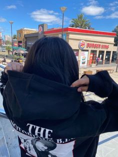 a woman with her back to the camera, covering her face and looking at shops