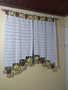 two white curtains hanging on the side of a wall next to a window with red, yellow and green flowers