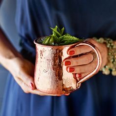 a woman holding a copper mug filled with green leaves