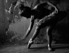 black and white photograph of a woman in ballet shoes leaning against a wall with her hands behind her head