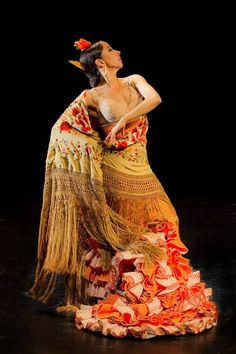 a woman in an orange and yellow dress on stage with her hands behind her back