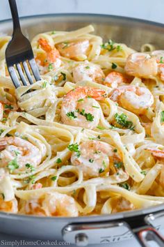 pasta with shrimp and parmesan cheese in a skillet being eaten by a fork