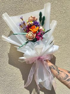 a person's arm with tattoos holding a bouquet of flowers and wrapped in cellophane