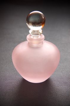 a pink glass bottle sitting on top of a black table next to a brown and white object