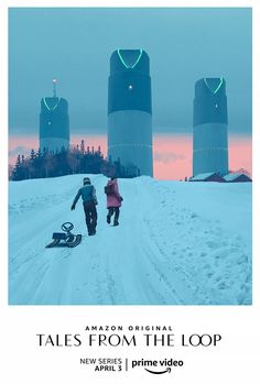 two people walking down a snowy road in front of three silos with neon lights