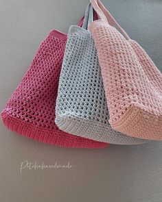 three crocheted purses hanging from hooks on the wall, one pink and one gray