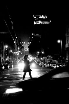 a woman crossing the street at night with her back to the camera as she crosses the street