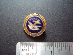 a gold and blue lapel pin with a cross on it next to a ruler