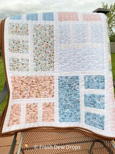 a quilted blanket sitting on top of a chair in front of a green field