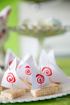 small sailboats on crackers are sitting on a plate next to a white cat