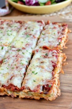 several slices of pizza sitting on top of a wooden cutting board next to a bowl of salad