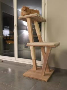 an orange cat laying on top of a wooden scratching post in front of a window