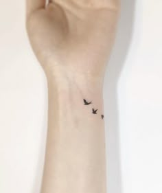 a small tattoo on the wrist of a woman with two birds flying in the sky