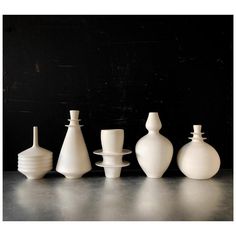 five white vases sitting on top of a table next to each other in front of a black wall