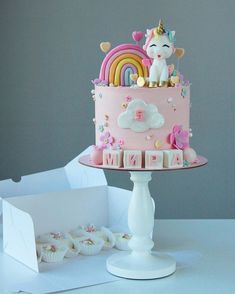 there is a pink cake with unicorns on it and cupcakes in the background