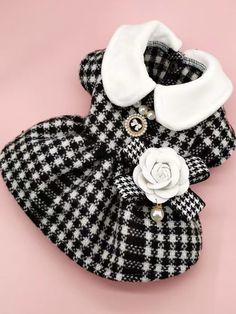 a black and white checkered dress with a flower on the collar is sitting on a pink surface