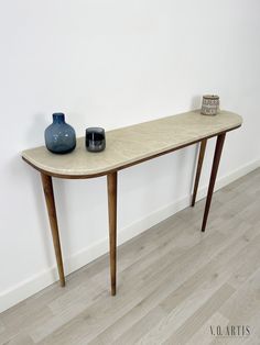 a table with two vases on it in front of a white wall and wood floor