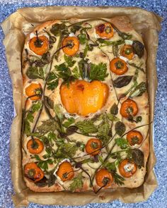 a square shaped pizza with oranges and herbs on it's crust, sitting on a blue surface